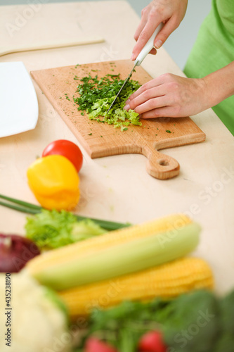 Unknown young woman slicing greens for a delicious fresh vegetarian salad while standing at the kitchen desk, just hands, close-up. Cooking concept