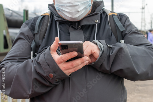 a man in a medical mask and a gray jacket types a message on his phone. hands in the frame