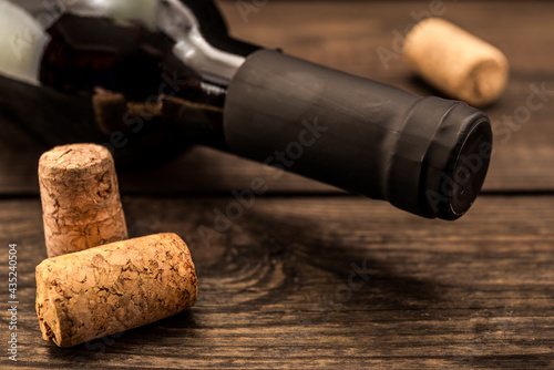 Bottle of red wine with corks lying on an old wooden table. Close up view, focus on the bottle of red wine