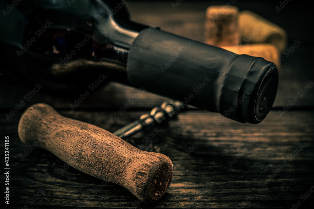 Bottle of red wine with corks and corkscrew lying on an old wooden table. Close up view, focus on the bottle of red wine