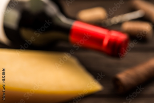 Bottle of red wine with a piece of parmesan and corkscrew with corks and cuban cigar lying on an old wooden table. Close up view, defocused image