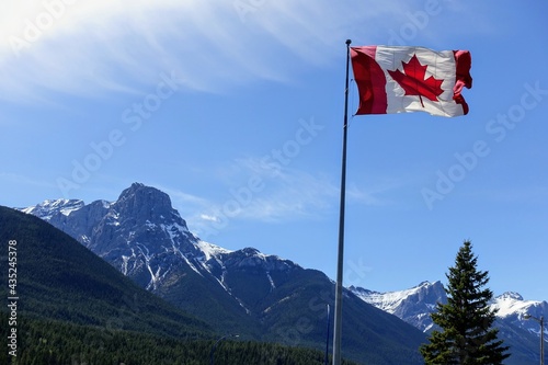 A photo of a huge canadian flag waving in the wind with the rocky mountains behind it on a beautiful sunny day