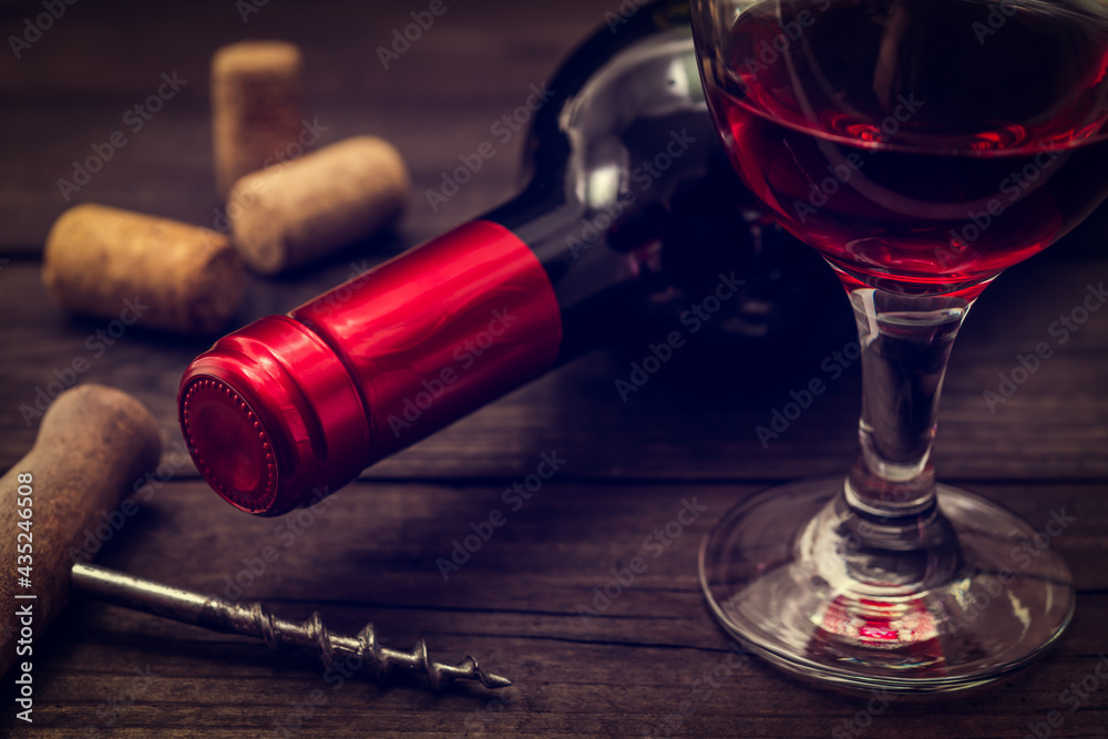 Bottle of red wine with a glass of red wine and corkscrew on an old wooden table. Close up view, focus on the bottle of red wine