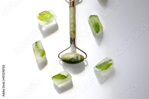 Green face roller and ice cubes on white background. Derma roller for skin care. photo