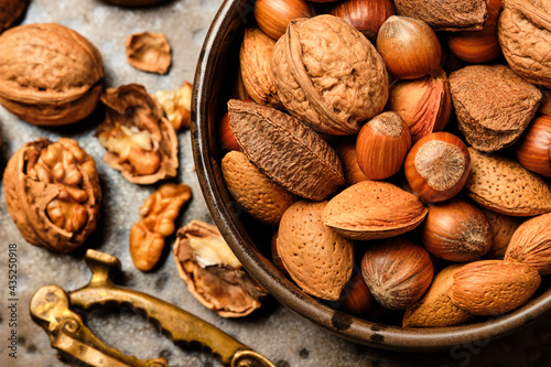 Almonds, walnuts and hazelnuts are sitting in a brown bowl and a nutcracker on a dark brown spotted plate.