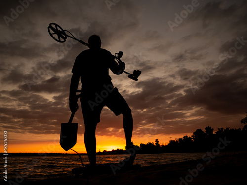 Silhouette of a man with a metal detector and a shovel against the sky. photo