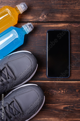 Layout of sports training concept, sneakers, smartphone and two bottles of isotonic drink on a dark wooden background, mockup.