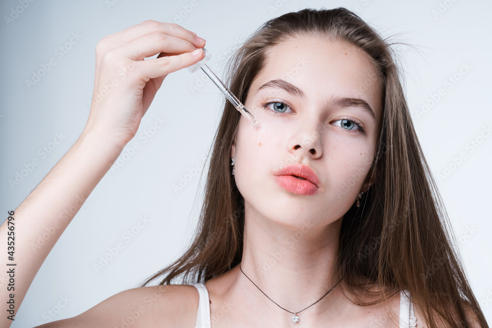A beautiful girl with clean skin applies serum to her face with a pipette. Skin care concept A beautiful girl with clean skin applies serum to her face with a pipette. Skin care concept