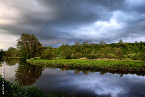 Fototapeta Naklejka Na Ścianę i Meble -  Stormy skies as the sun sets over the River Wey and meadows in Godalming, Surrey, UK