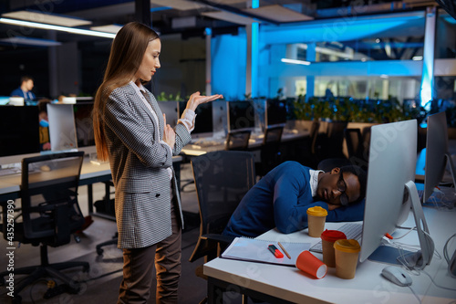 Woman looks on sleeping manager, night office