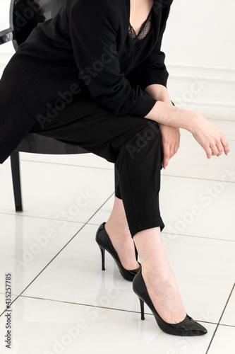 Pretty young woman in black business suit and high-heeled shoes sits on the stool , body part close up