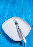 Close-up of empty squared white ceramic plate and silver cutlery on blue wooden boards. Copyspace. Vertical photo.