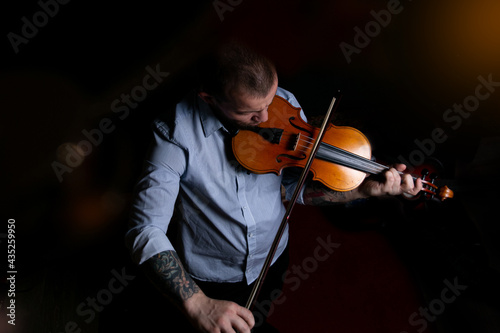 A man in a blue shirt plays the violin on a black background