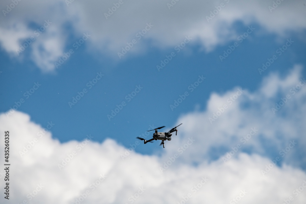 a soaring drone flies above the ground against the background of a blue and white sky a soaring drone flies above the ground against the background of a blue and white sky