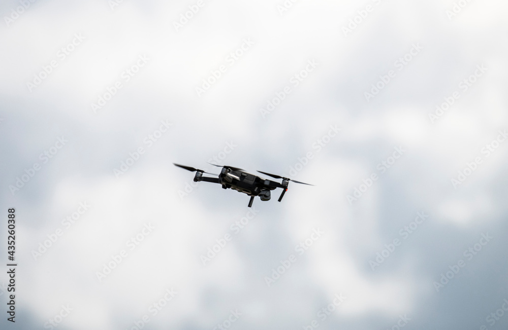 a soaring drone flies above the ground against the background of a blue and white sky