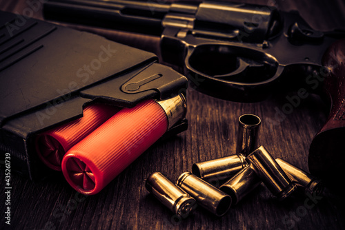 Magazines with red cartridges 12 gauge and revolver on the wooden table. Close up view