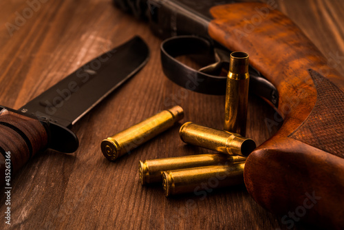 Empty shells with rifle and combat knife lying on a wooden table. Close up view, focus on the shells