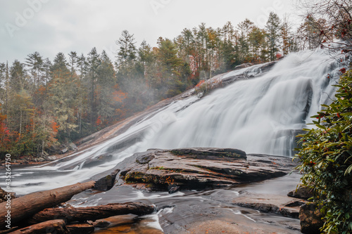 Fototapeta Naklejka Na Ścianę i Meble -  Lower views of the High Falls waterfall of the Little River cascading down rocks surrounded by colorful fall foliage on a foggy, misty morning in DuPont State Recreational Forest, North Carolina, USA.