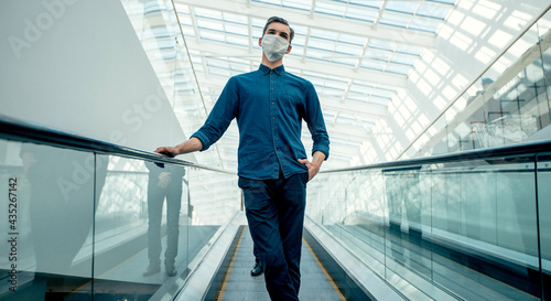 young man in a protective mask standing on the escalator steps.