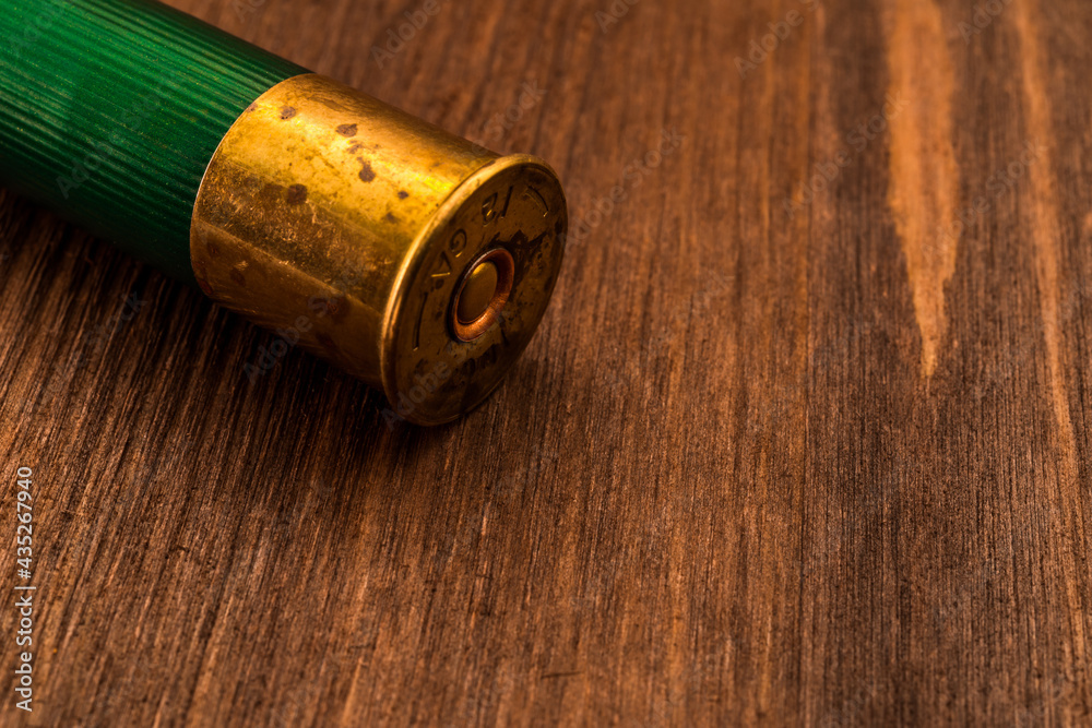 One 12 gauge cartridge lying on a wooden table. Close up view