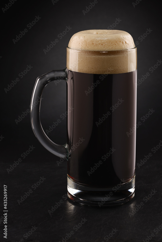 Stein with fresh stout beer with cap of foam on a black. - obrazy, fototapety, plakaty 