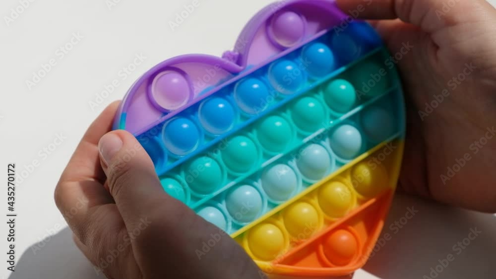 Hands play with antistress pop it toy. Rainbow sensory fidget isolated on white background. New trendy silicone toy. Hands play with antistress pop it toy. Rainbow sensory fidget isolated on white background. New trendy silicone toy.
