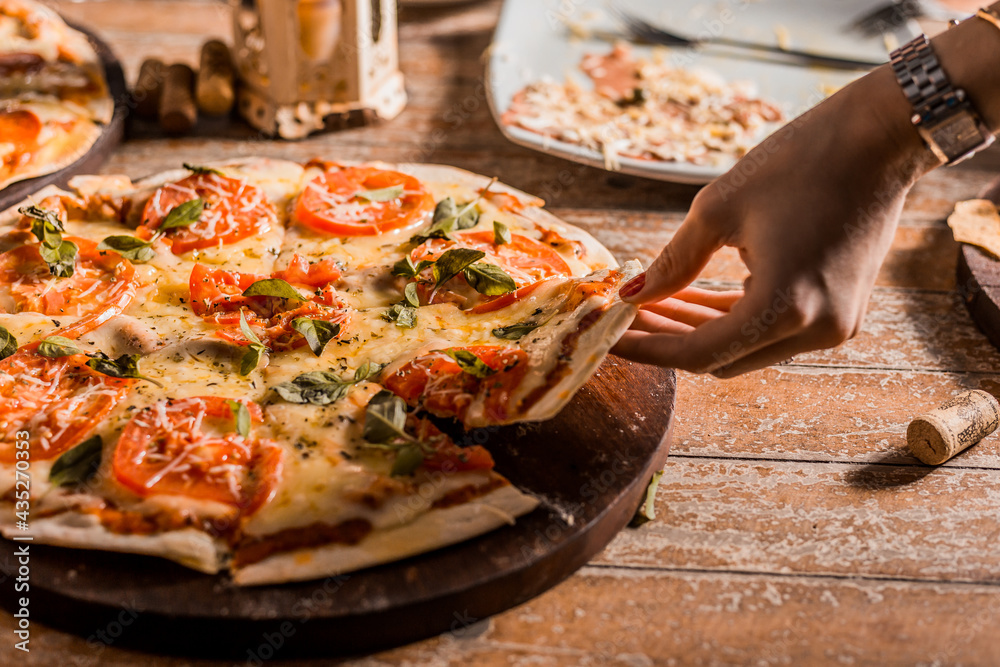 Female Hands Grabs a beautiful Pizza Slice with melted cheese on a wooden table
