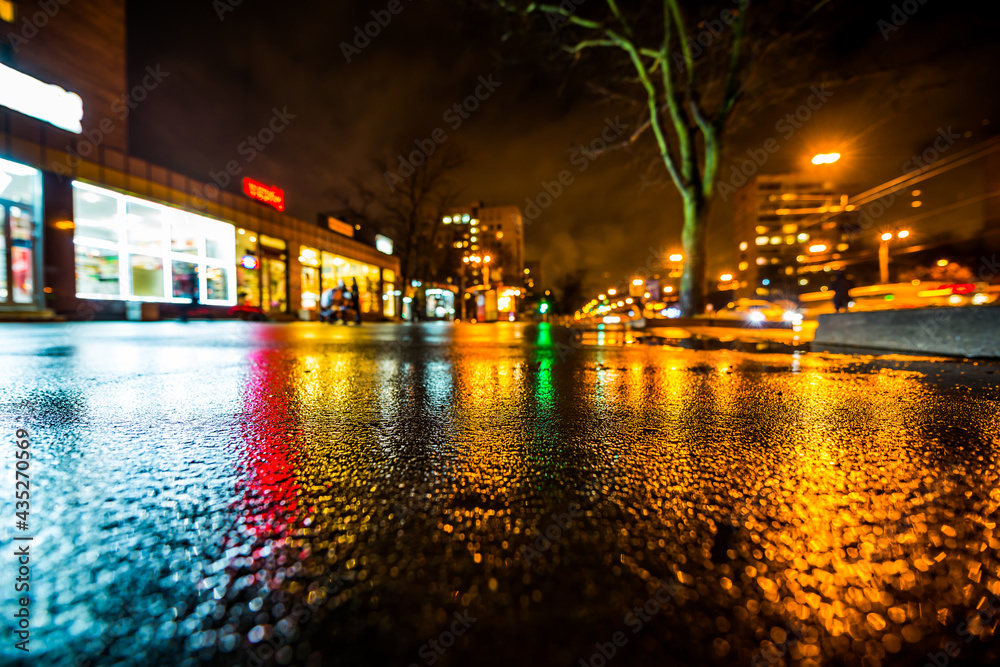 Rainy night in the big city, city street, in the light of shop windows. View from a wide angle at the level of asphalt