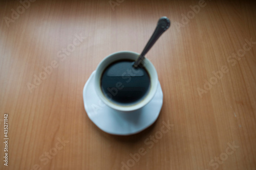 Taza blanca de café negro con cucharita sobre mesa de madera clara vista desde arriba photo