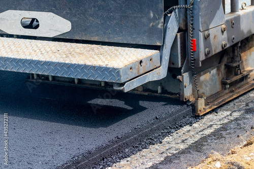 Asphalt paver on the road while laying asphalt, part of the car close up. Road repair. Laying a new road