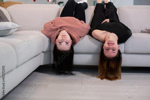 Two young girls merrily lie on the couch with their legs up, staring at the camera. The concept of youth and friendship. High quality photo