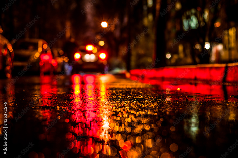 Obraz premium Rainy night in the big city, alley between houses with a car traveling. View from the level of asphalt