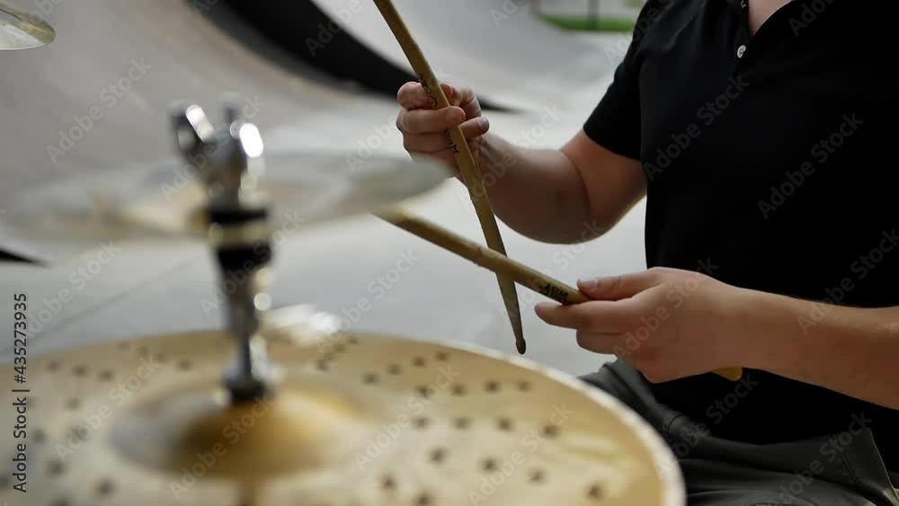 Close-up of the hands of a drummer twirling drumsticks between his fingers during an outdoor rock concert. A man prepares for a performance sitting at a drum kit during an open air concert.