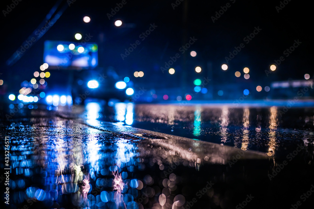 Rainy night in the big city, the light from the headlamps of approaching car on the highway. View from the level of the dividing line
