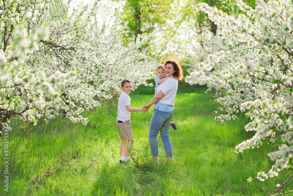 rear view.mother with sons walks in flowering garden. youngest child in her arms rear view.mother with sons walks in flowering garden. youngest child in her arms
