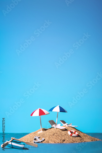 Fototapet Still life shot of an island with two umbrellas, two sunbeds , a life preserver,
