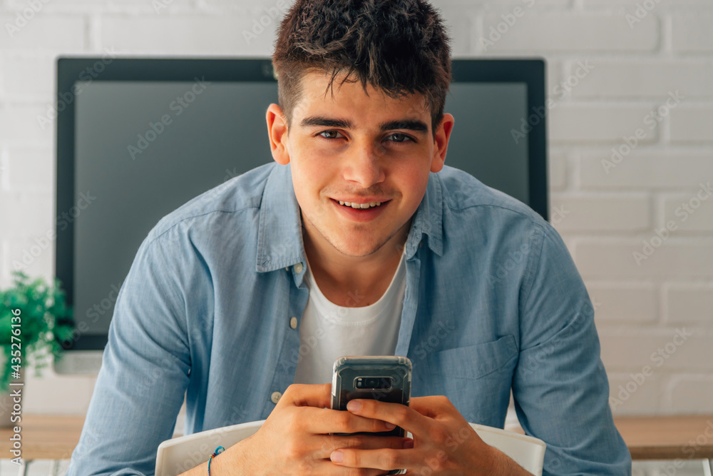 portrait of young teenager with mobile phone in hands and computer in the background