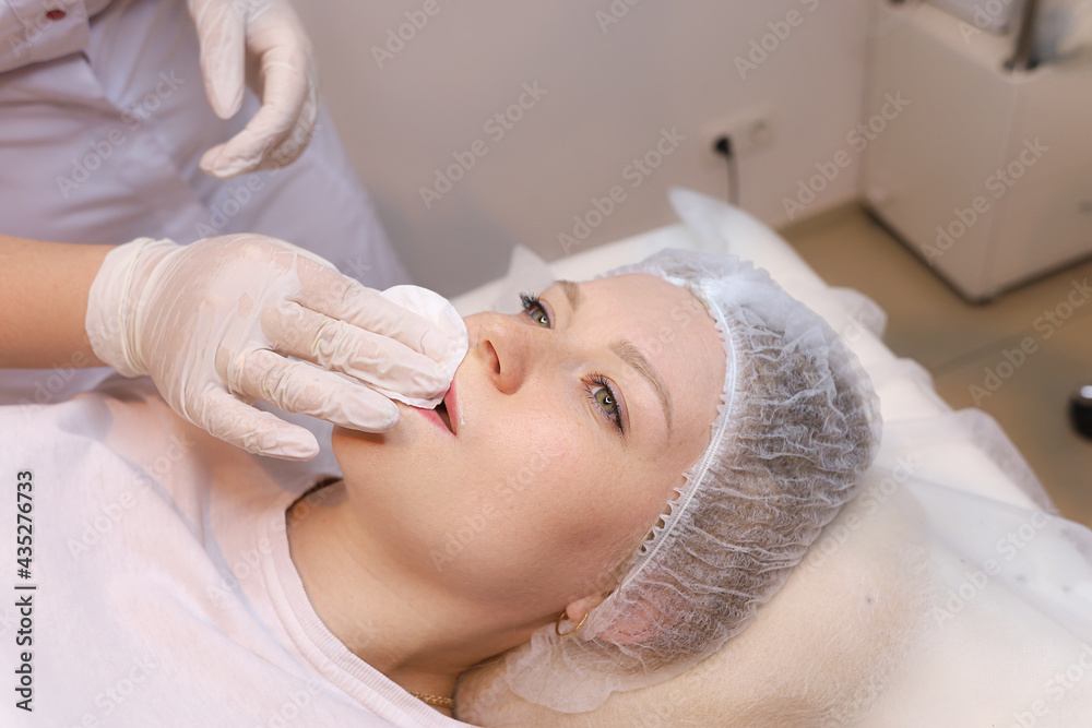 The cosmetologist wipes the remnants of anesthesia from the client's lips with a cotton sponge