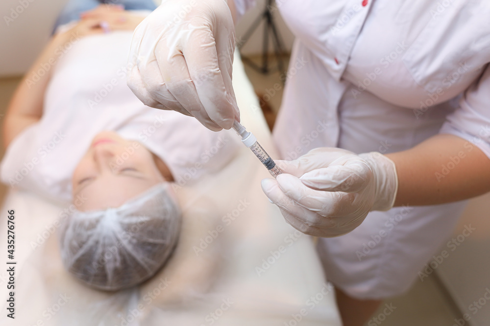 Naklejka premium The cosmetologist holds the filler for injections of hyaluronic acid and removes the protective cap from the needle
