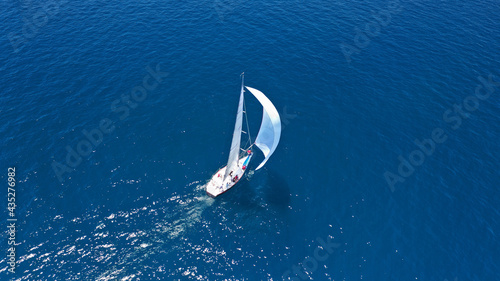 Aerial drone top down photo of beautiful sail boat with trained crew cruising in deep blue Aegean sea