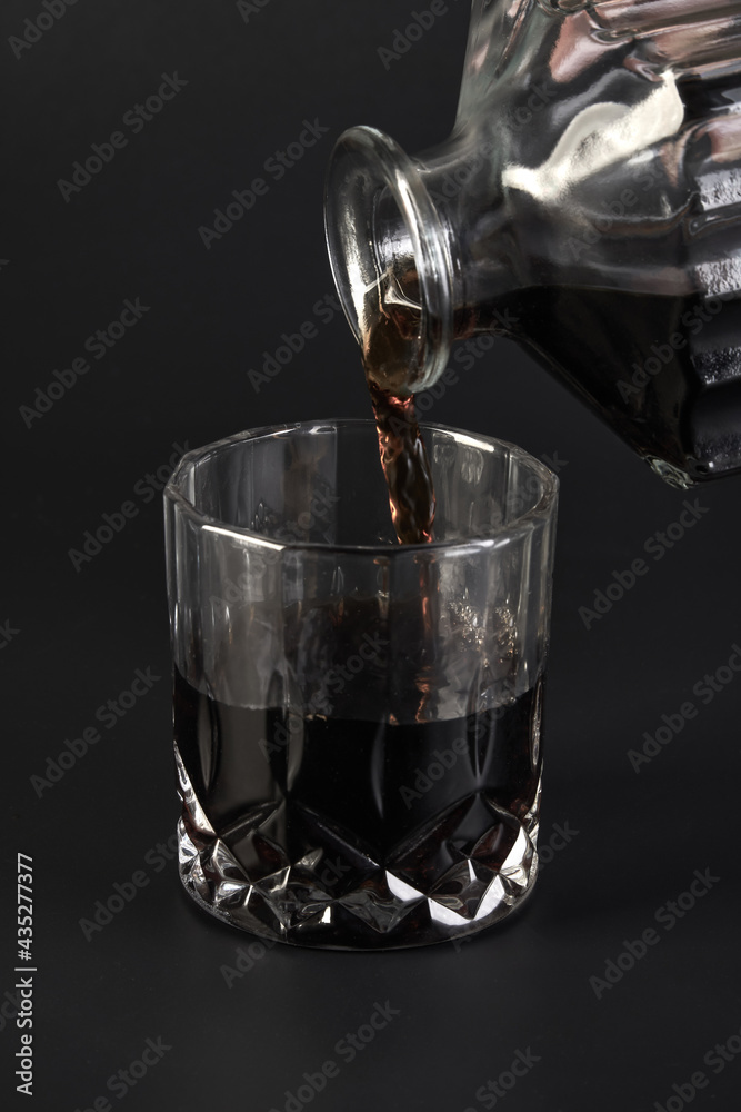 Someone pours cognac from a square decanter into a glass on a dark background