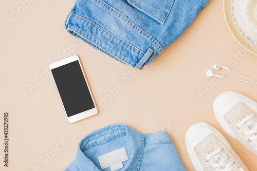 Flat lay summer composition with a straw hat, jeans and sneakers on a yellow background