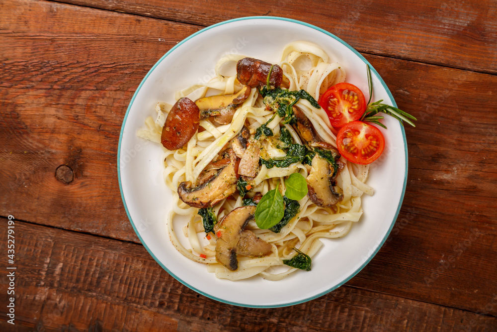 Udon with mushrooms and spinach and cherry tomatoes in a plate on a wooden table. Udon with mushrooms and spinach and cherry tomatoes in a plate on a wooden table.