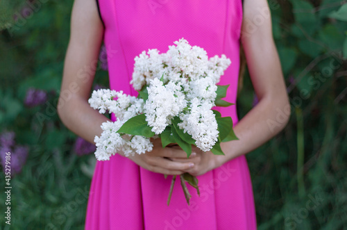 a girl in a purple dress holds a bouquet of white lilacs flowers