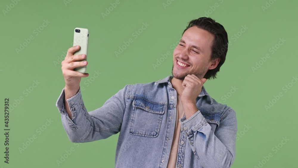 Handsome happy cheery young brunet blue eyed man 20s years old wears denim shirt posing doing selfie shot on mobile phone post photo on social network isolated on pastel green color background studio Handsome happy cheery young brunet blue eyed man 20s years old wears denim shirt posing doing selfie shot on mobile phone post photo on social network isolated on pastel green color background studio