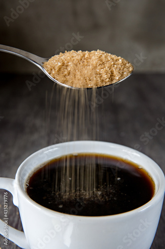 Raw sugar being put into a cup of coffee  photo