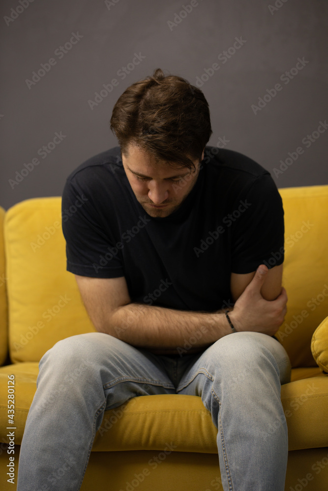 unshaven handsome guy sits on sofa suffering from stomach ache at home. Grabbing and squeezing belly with hands, feeling exhausted. abdominal pain. Food poisoning, Painkillers, pain pills. unshaven handsome guy sits on sofa suffering from stomach ache at home. Grabbing and squeezing belly with hands, feeling exhausted. abdominal pain. Food poisoning, Painkillers, pain pills.