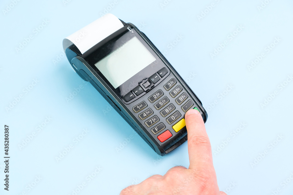 Man hand pushing a button on POS terminal with roll paper cash tape on the blue background Man hand pushing a button on POS terminal with roll paper cash tape on the blue background