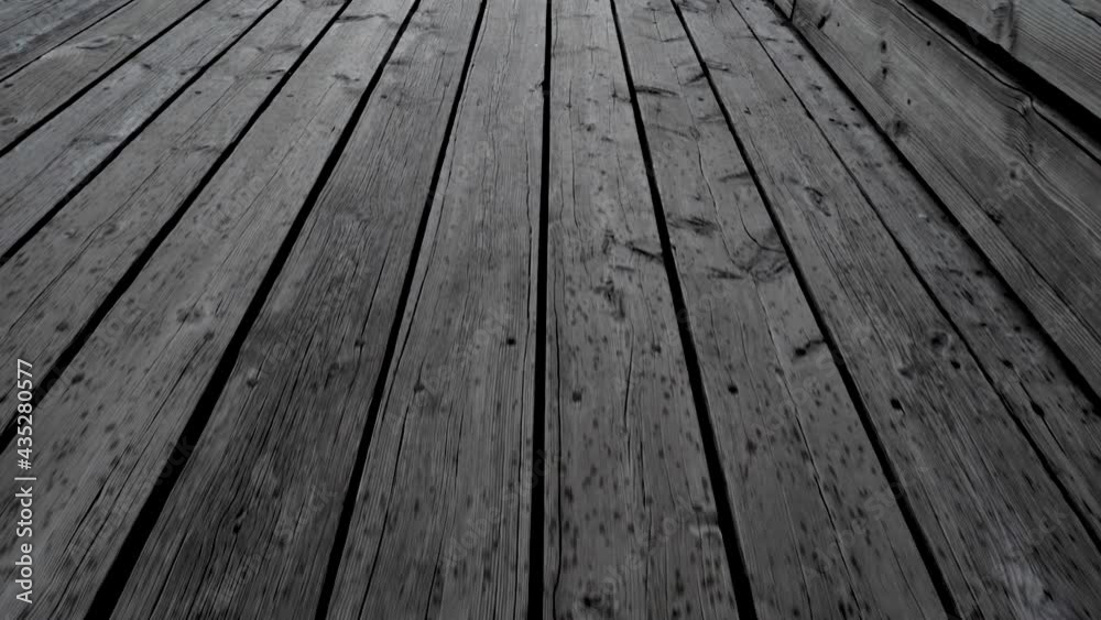 Bouncing walk on wooden quay. Coarse wide planks that are fastened with large nails. You can see the water between the planks in some places. Raindrops have created dark spots on the quay. Bouncing walk on wooden quay. Coarse wide planks that are fastened with large nails. You can see the water between the planks in some places. Raindrops have created dark spots on the quay.