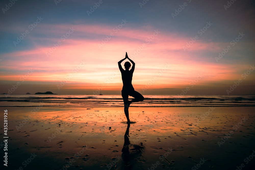 Yoga woman meditation on the amazing sunset sea coast with reflection in water.